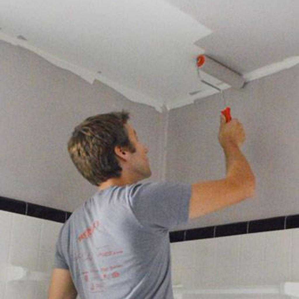 мужчина красит потолок в ванной комнате